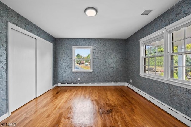 unfurnished bedroom featuring a baseboard radiator, a closet, and hardwood / wood-style floors