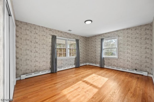 empty room with a baseboard heating unit, hardwood / wood-style floors, and plenty of natural light