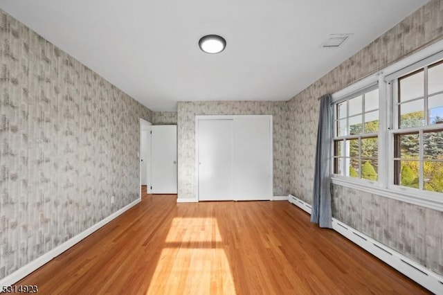 unfurnished bedroom featuring baseboard heating, a closet, and light hardwood / wood-style flooring