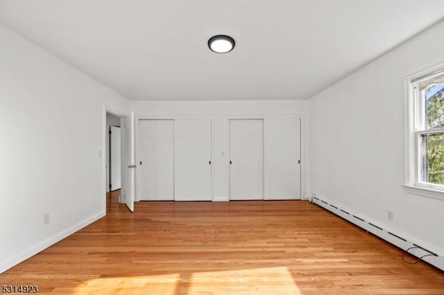 unfurnished bedroom featuring a baseboard heating unit, light hardwood / wood-style floors, and multiple closets