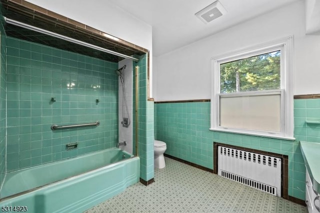 bathroom with tile walls, toilet, tiled shower / bath combo, and radiator