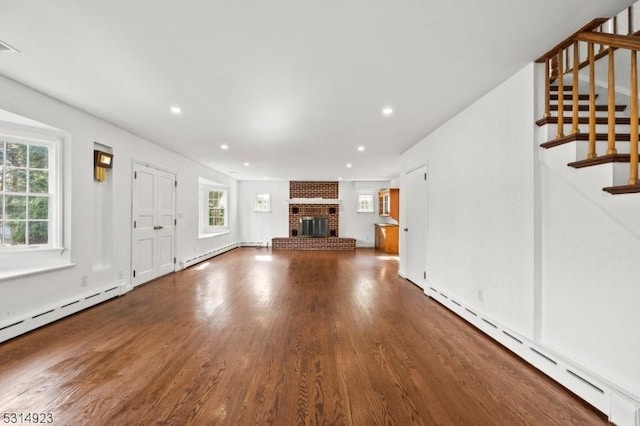 unfurnished living room with wood-type flooring, a baseboard radiator, and a brick fireplace