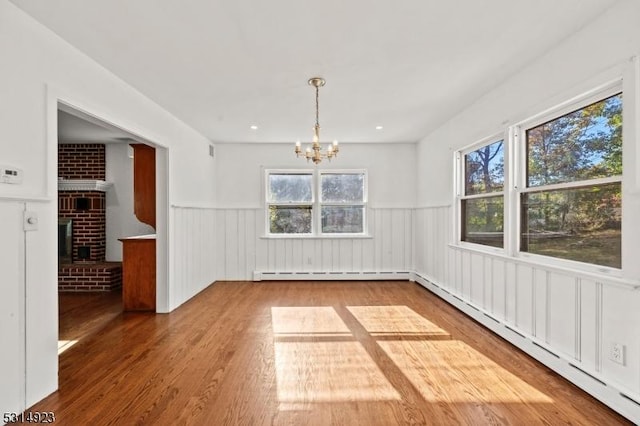 unfurnished dining area with a baseboard radiator, a fireplace, hardwood / wood-style flooring, and a notable chandelier