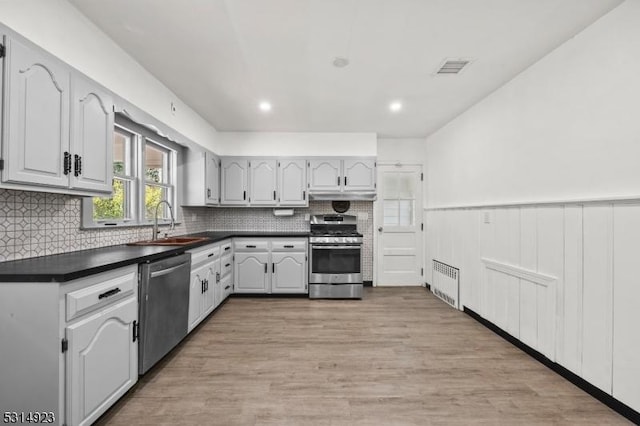 kitchen featuring stainless steel appliances, sink, white cabinets, light hardwood / wood-style flooring, and radiator heating unit