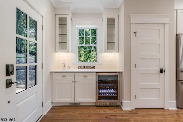 bar with wine cooler, white cabinets, light wood-type flooring, and stainless steel fridge