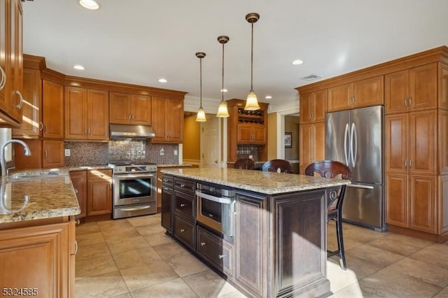 kitchen featuring a center island, sink, stainless steel appliances, light stone counters, and pendant lighting