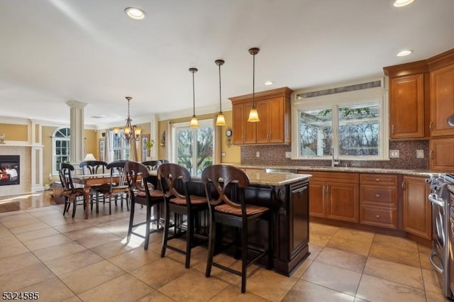 kitchen featuring light stone counters, ornate columns, a kitchen island, hanging light fixtures, and a breakfast bar area