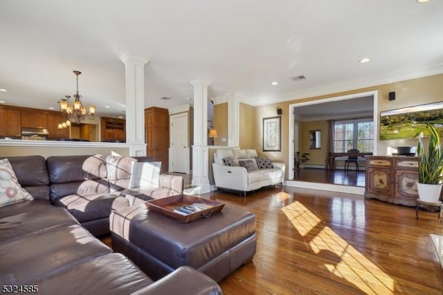 living room with hardwood / wood-style floors, an inviting chandelier, ornamental molding, and decorative columns