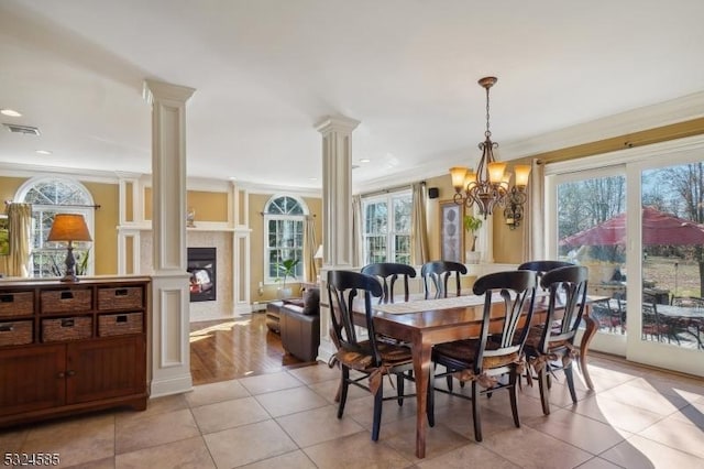 tiled dining area with a healthy amount of sunlight, ornate columns, crown molding, and a notable chandelier