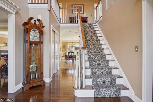 staircase featuring crown molding, a towering ceiling, and wood-type flooring