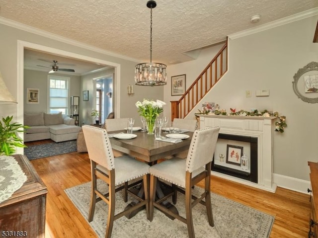 dining room with light wood-type flooring, a textured ceiling, crown molding, baseboards, and a chandelier