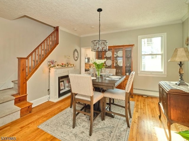 dining room with a baseboard heating unit, stairway, ornamental molding, light wood-style floors, and a textured ceiling