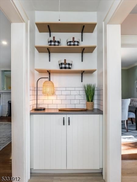 bar with backsplash, light hardwood / wood-style flooring, and white cabinetry