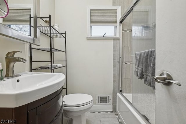 full bathroom featuring sink, combined bath / shower with glass door, toilet, and a healthy amount of sunlight