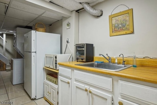 kitchen with a drop ceiling, white fridge, sink, light tile patterned flooring, and white cabinets