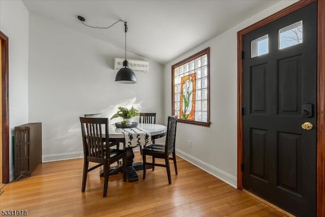 dining area featuring radiator heating unit, a wall mounted AC, light hardwood / wood-style flooring, and lofted ceiling