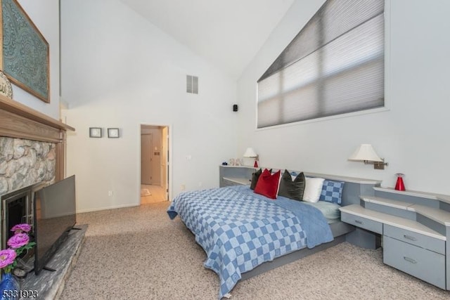 carpeted bedroom featuring a stone fireplace and high vaulted ceiling