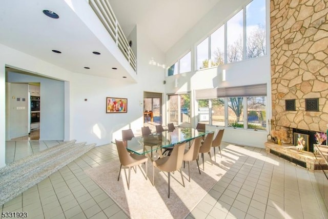 tiled dining space with a towering ceiling and a stone fireplace