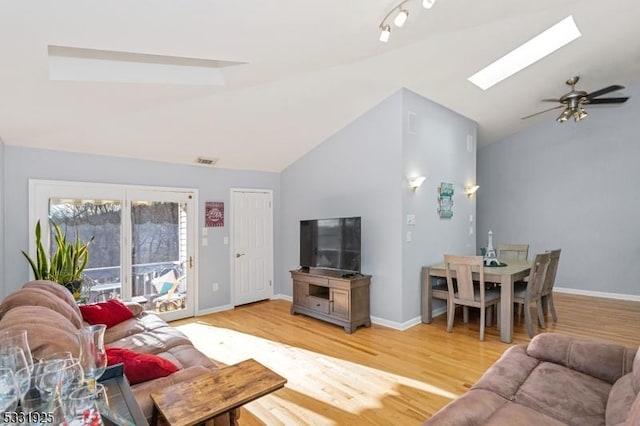 living room with light hardwood / wood-style flooring, ceiling fan, and vaulted ceiling with skylight