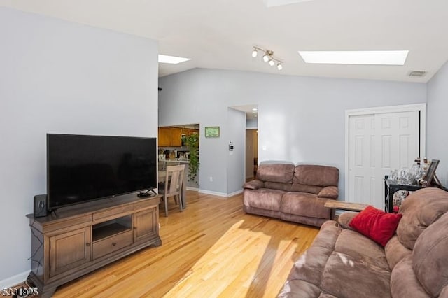 living room featuring vaulted ceiling with skylight and light hardwood / wood-style floors