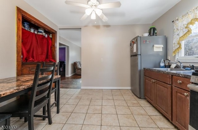 kitchen with ceiling fan, sink, dark stone countertops, stainless steel refrigerator, and light tile patterned flooring