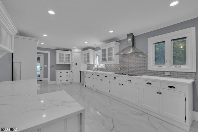 kitchen featuring sink, wall chimney exhaust hood, tasteful backsplash, light stone counters, and white cabinets