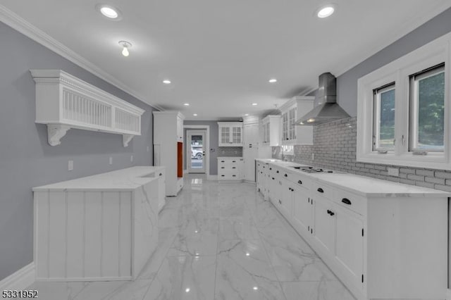 kitchen with decorative backsplash, ornamental molding, white gas stovetop, wall chimney range hood, and white cabinets