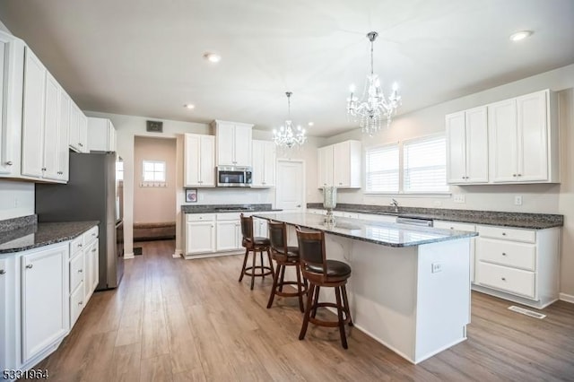 kitchen with dark stone countertops, a center island with sink, light hardwood / wood-style floors, pendant lighting, and white cabinetry