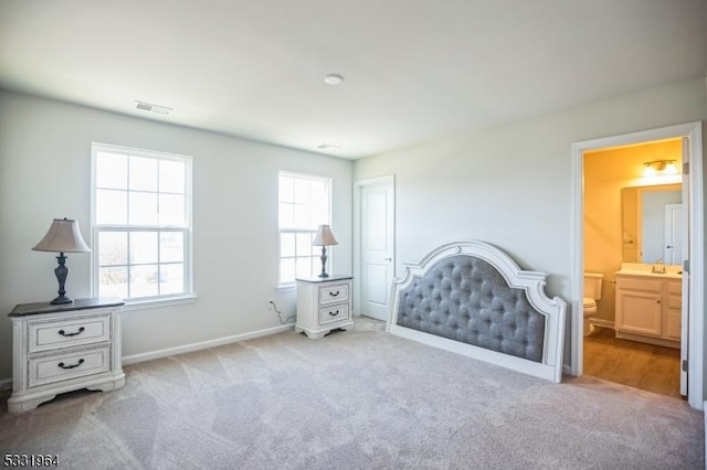 bedroom featuring ensuite bathroom, light carpet, and sink