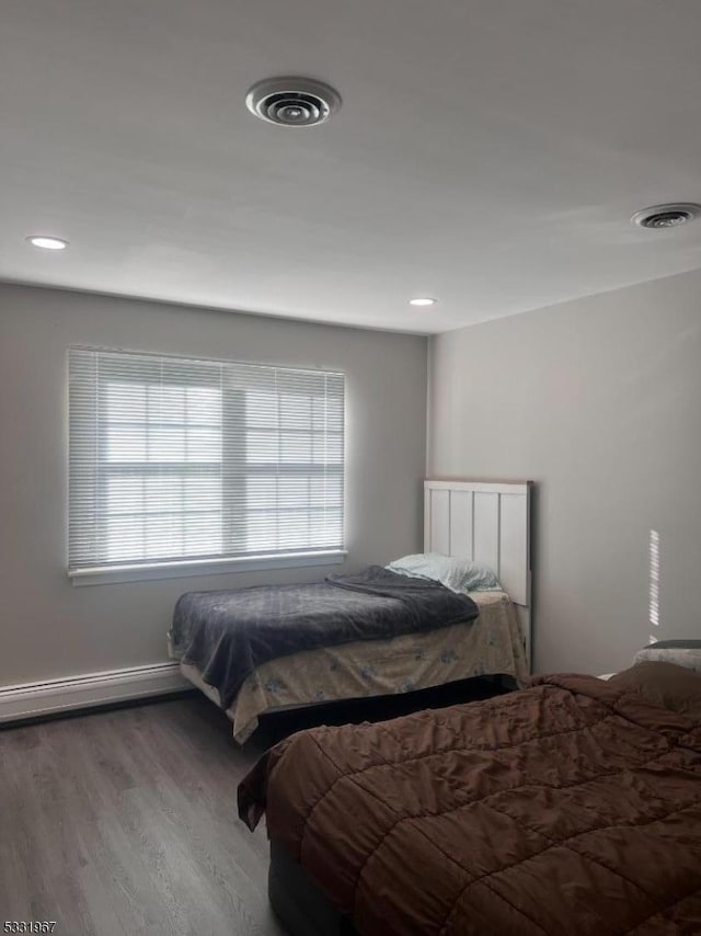 bedroom featuring hardwood / wood-style floors, a baseboard radiator, and multiple windows