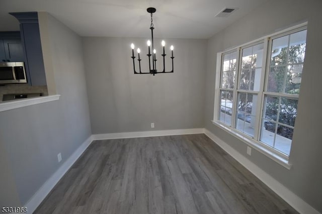 unfurnished dining area with dark wood-type flooring, a healthy amount of sunlight, and a notable chandelier