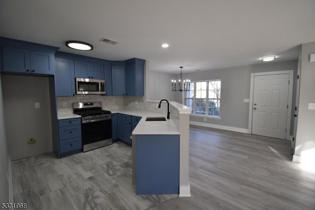 kitchen with kitchen peninsula, appliances with stainless steel finishes, sink, pendant lighting, and a notable chandelier