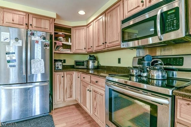 kitchen featuring appliances with stainless steel finishes, light hardwood / wood-style flooring, and dark stone counters