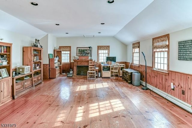 interior space with a healthy amount of sunlight, vaulted ceiling, wooden walls, and light hardwood / wood-style flooring