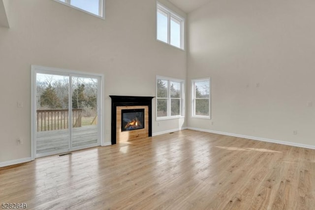 unfurnished living room featuring plenty of natural light, a towering ceiling, and light hardwood / wood-style flooring