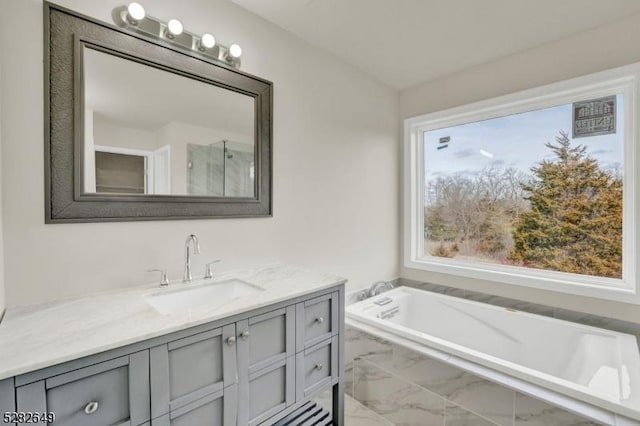 bathroom with vanity, a relaxing tiled tub, and plenty of natural light