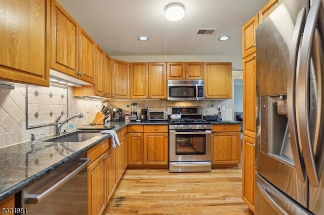 kitchen with sink, stainless steel appliances, tasteful backsplash, dark stone countertops, and light hardwood / wood-style floors