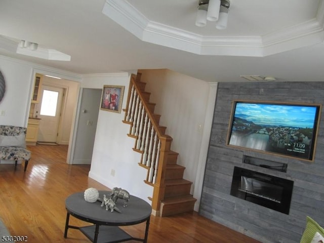 living room with a raised ceiling, a fireplace, wood-type flooring, and ornamental molding