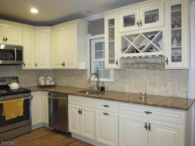 kitchen with sink, tasteful backsplash, dark stone counters, white cabinets, and appliances with stainless steel finishes