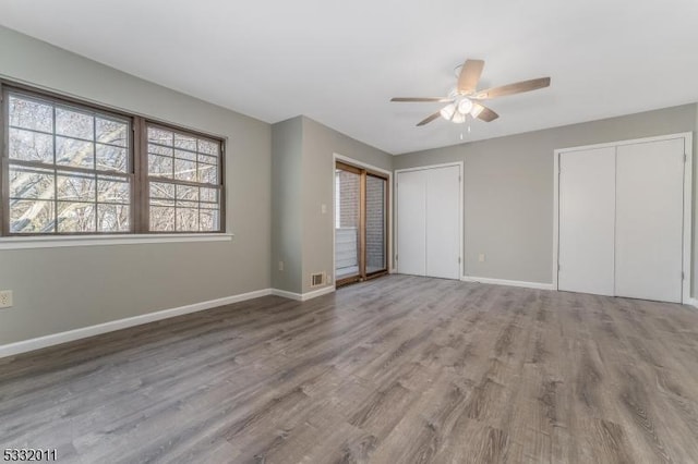 unfurnished bedroom featuring ceiling fan, wood-type flooring, and multiple closets