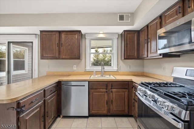 kitchen with dark brown cabinetry, sink, kitchen peninsula, light tile patterned floors, and appliances with stainless steel finishes