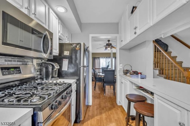 kitchen with backsplash, stainless steel appliances, ceiling fan, light hardwood / wood-style floors, and white cabinetry