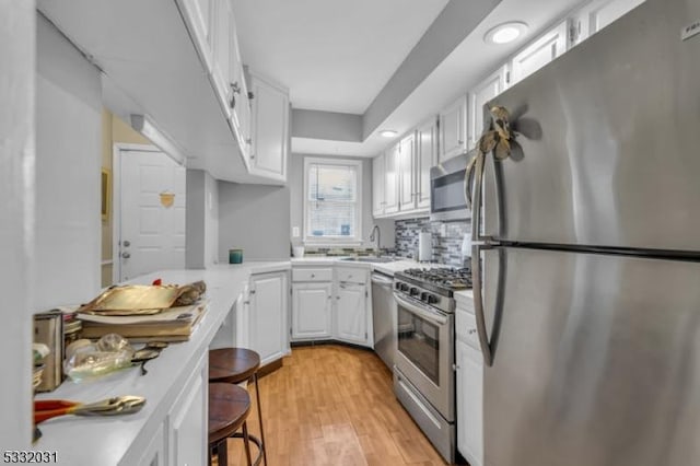 kitchen with stainless steel appliances, a kitchen breakfast bar, tasteful backsplash, light hardwood / wood-style flooring, and white cabinets