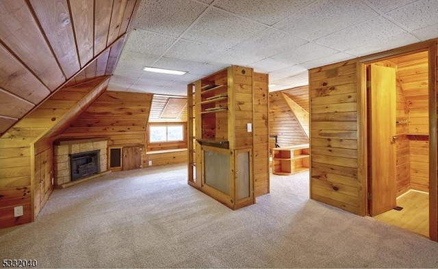 bonus room with lofted ceiling, light colored carpet, a stone fireplace, and wooden walls