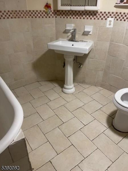 bathroom featuring toilet, tile patterned floors, tile walls, and sink