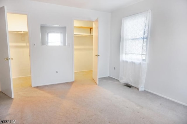 unfurnished bedroom featuring a walk in closet, a closet, and light colored carpet