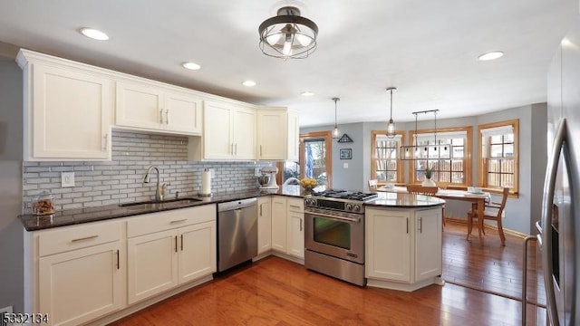 kitchen with kitchen peninsula, wood-type flooring, sink, decorative light fixtures, and stainless steel appliances