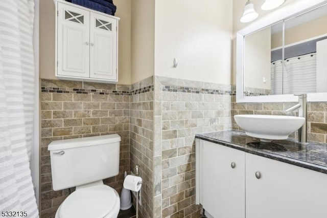 bathroom with toilet, wainscoting, vanity, and tile walls