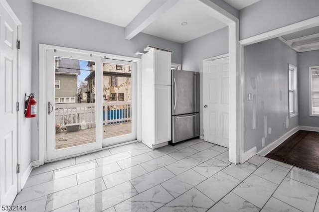 kitchen with plenty of natural light, beamed ceiling, white cabinets, and stainless steel refrigerator