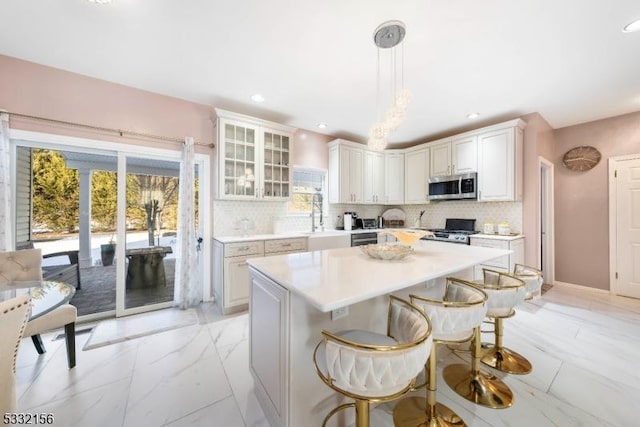 kitchen featuring a kitchen breakfast bar, stainless steel appliances, white cabinets, a center island, and hanging light fixtures